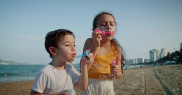 Счастливые дети, играющие с мыльными пузырями. Портретная улыбка довольно кавказских маленьких детей. Брат и сестра лопают мыльные пузыри. Детские игры на свежем воздухе — стоковое видео