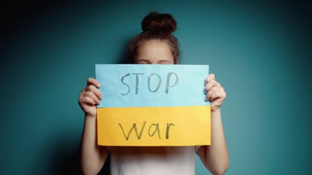 Ukraynalı zavallı çocuk korkmuş evsiz kız savaş çatışmasını protesto ediyor. Afişi yazı ile kaldırıyor. Mavi arka planda savaş yok. Barış, saldırganlığı bırak, çocuk Rus savaşına karşı. — Stok video
