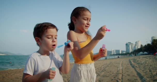Enfants heureux jouant avec des bulles de savon.Enfants heureux sourire souffler des bulles sur la plage. Portrait sourire assez petits enfants caucasiens. Frère et sœur éclatent des bulles de savon. Enfants jeu de jeu extérieur — Video