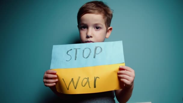 Ukraynalı zavallı çocuk korkmuş çocuk savaş savaşını protesto eden evsiz çocuk afişi yazı ile yükseltti mavi arka planda savaş yok. Barış, saldırganlığı bırak, çocuk Rus savaşına karşı. — Stok video