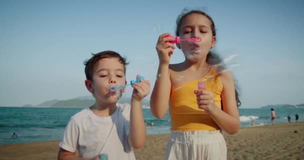 Happy Children spelen met zeepbellen.Kinderen blij glimlach blazen bellen op het strand. Portret glimlach vrij Kaukasische kleine kinderen. Broer en zus barsten van zeepbellen. Kinderen buiten spel spelen — Stockvideo