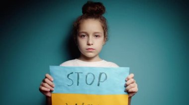 Ukraynalı zavallı çocuk korkmuş evsiz kız savaş çatışmasını protesto ediyor. Afişi yazı ile kaldırıyor. Mavi arka planda savaş yok. Barış, saldırganlığı bırak, çocuk Rus savaşına karşı.