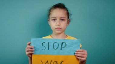 Ukraynalı zavallı çocuk korkmuş evsiz kız savaş çatışmasını protesto ediyor. Afişi yazı ile kaldırıyor. Mavi arka planda savaş yok. Barış, saldırganlığı bırak, çocuk Rus savaşına karşı.