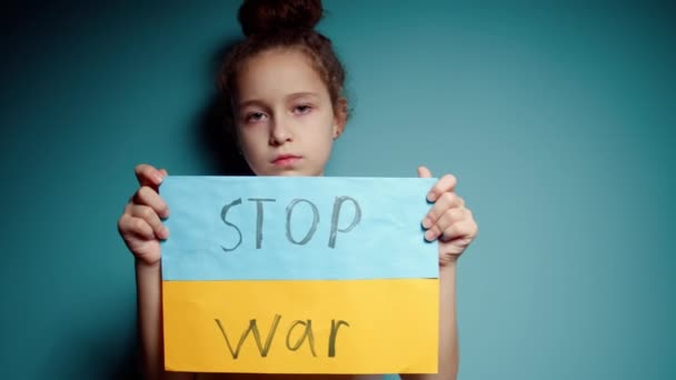 Molesto ucraniano pobre niño asustado niña sin hogar protestar conflicto de guerra levanta pancarta con texto de masaje inscripción No War on blue background. Paz, detener la agresión, niño contra la guerra rusa — Vídeos de Stock