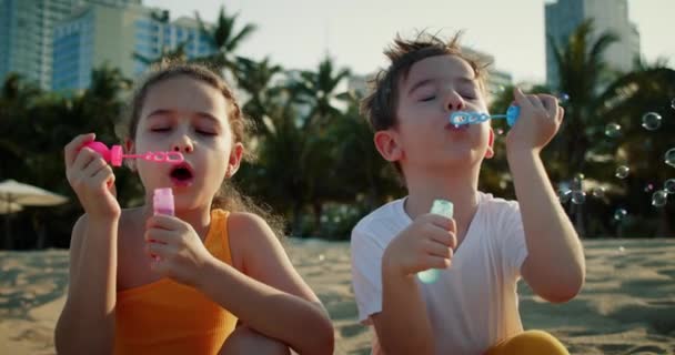 Happy Children leker med såpbubblor.Kids glada leende blåser bubblor på stranden. Porträtt leende ganska kaukasiska små barn. Broder och syster spräcker såpbubblor. Barnens utomhus lek spel — Stockvideo