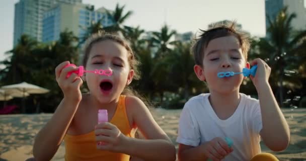 Glückliche Kinder, die mit Seifenblasen spielen.Glückliches Lächeln der Kinder Blasen am Strand pusten. Porträt lächeln hübsche kaukasische kleine Kinder. Bruder und Schwester platzen Seifenblasen. Spiele Kinder im Freien spielen — Stockvideo