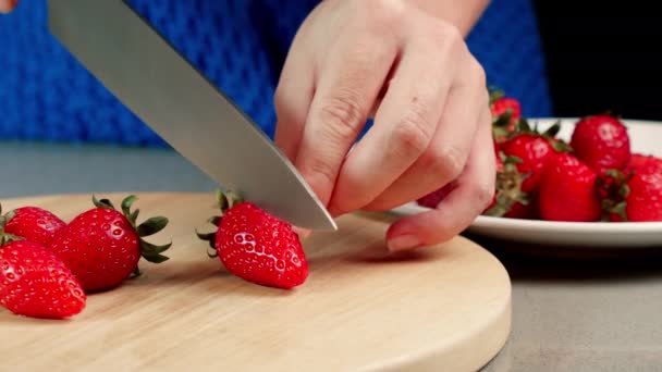 Oigenkännliga kvinna händer skära läckra söta jordgubbar i skivor på trä bricka med färska frukter och bär. Flicka förbereda hälsosam frukost glasbord i köket närbild — Stockvideo