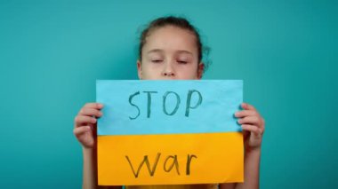 Ukraynalı zavallı çocuk korkmuş evsiz kız savaş çatışmasını protesto ediyor. Afişi yazı ile kaldırıyor. Mavi arka planda savaş yok. Barış, saldırganlığı bırak, çocuk Rus savaşına karşı.