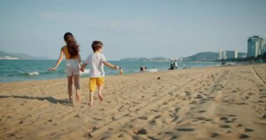 Mutlu beyaz çocuklar plaj boyunca koşar. Küçük çocuklar, erkek ve kız kardeşler plajda koşuyorlar, oynuyorlar, aile tatili yapıyorlar. Küçük çocuklar için bir plaj tatili konsepti