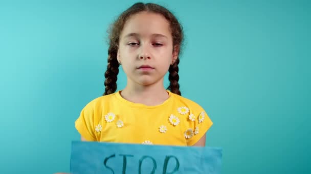Ukraynalı zavallı çocuk korkmuş evsiz kız savaş çatışmasını protesto ediyor. Afişi yazı ile kaldırıyor. Mavi arka planda savaş yok. Barış, saldırganlığı bırak, çocuk Rus savaşına karşı. — Stok video