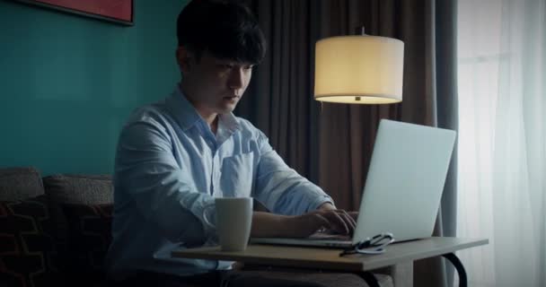 Trøtt kontoransatt tar av seg briller, hviler fra skrivebordsarbeid. Ung, attraktiv asiatisk vietnamesisk mann er opptatt med å jobbe med lærdom på skrivebordsbok hos hjemmedataanalytiker, forskning på data. – stockvideo
