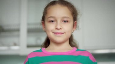 Kanepede oturan güzel yüzlü şirin çocuk portresi. Komik küçük kız kameraya bakıp gülümseyen çocuk evdeki kanepede oturuyor. Mutlu bir çocukluk kavramı.