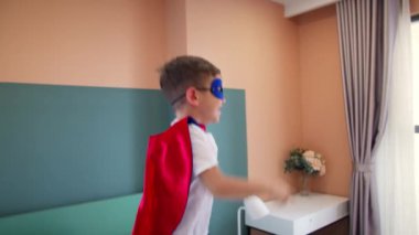 Kırmızı ve mavi Süpermen kostümlü çocuk, yatakta, çocuk odasında zıplayan süper kahraman çocuk. Süper kahramanlar, küçük kardeş, kendinizi süper kahraman olarak hayal edin..