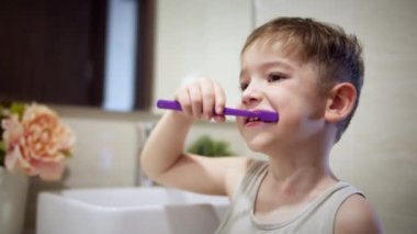 Çocuk günlük sağlık hizmeti rutini. Banyoda dişlerini fırçalayan ve gülümseyen mutlu küçük bir çocuk portresi. Beyaz dişli beyaz dişli beyaz çocuk evde izole edilmiş aynaya bakıyor. Yaşam biçimi.