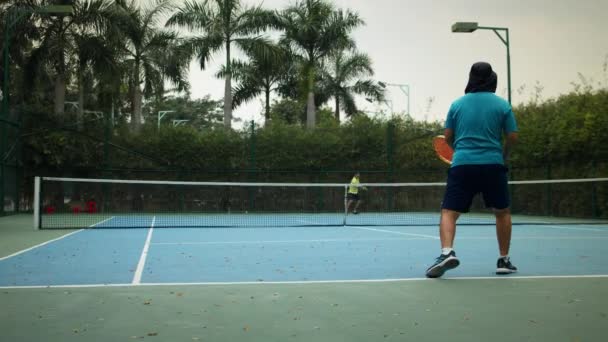 Los hombres asiáticos vestidos con trajes azules de tenis pasan tiempo en la cancha, jugando al tenis en un día soleado, sosteniendo una raqueta de tenis, golpeando una pelota de tenis en cámara lenta.Asia, Saigón, Vietnam, 6 de abril de 2022 — Vídeos de Stock