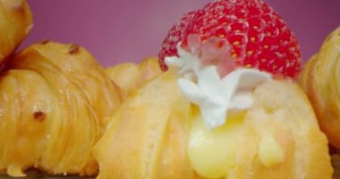 Kremalı ve çilekli donutlar koyu pembe arka planda, makro lensler tatlı tatlılar arasından geçiyor, ilginç düşük perspektifli.