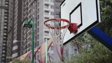 Spor basket potasına farklı açılardan atıyor. Basketbol sahasında basketbol potasından geçiyor. Arka planda şehir gökdelenleri. Saygon, Vietnam, 6 Nisan 2022