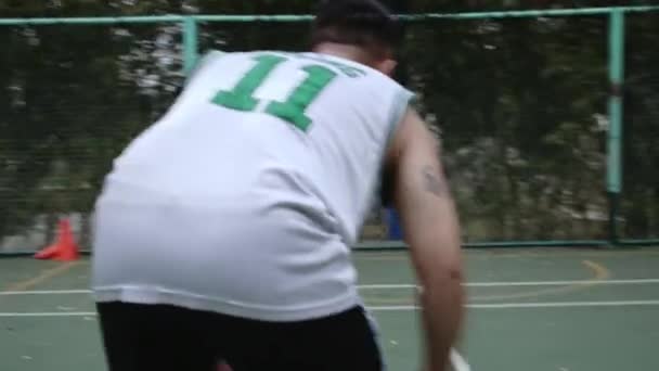 Jugador de baloncesto entrenando en el campo de baloncesto en el parque, el jugador golpea la pelota, luego lanza la pelota y golpea el ring y anota. — Vídeos de Stock