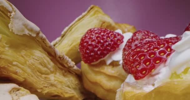 Kremalı ve çilekli donutlar koyu pembe arka planda, makro lensler tatlı tatlılar arasından geçiyor, ilginç düşük perspektifli. — Stok video