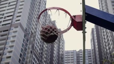 Spor basket potasına farklı açılardan atıyor. Basketbol sahasında basketbol potası, basketbol potası bulutları. Arka planda şehir gökdelenleri.