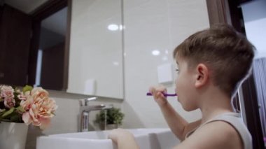 Çocuk günlük sağlık hizmeti rutini. Banyoda dişlerini fırçalayan ve gülümseyen mutlu küçük bir çocuk portresi. Beyaz dişli beyaz dişli beyaz çocuk evde izole edilmiş aynaya bakıyor. Yaşam biçimi.