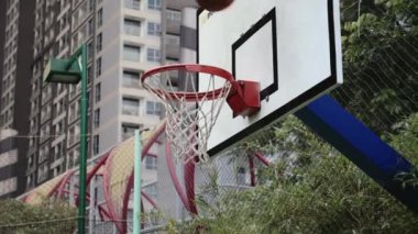Spor basket potasına farklı açılardan atıyor. Basketbol sahasında basketbol potasından geçiyor. Arka planda şehir gökdelenleri..