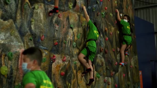 As crianças estão treinando na parede de escalada com um instrutor. Crianças escalada em rocha na escola privada.Exercícios de escalada.Crianças em idade escolar escalam parede de escalada.Saigão, Vietnã, 6 de abril de 2022 — Vídeo de Stock
