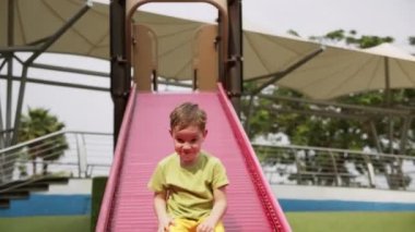 Çocuk mutlu bir şekilde gülüyor, çocuk parkında kayıyor, küçük çocuk güneşli bir günde parkta sallanıyor, neşeli çocuklar tepeden tırnağa geziyor, çocuk şehir parkında oynarken gülüyor.