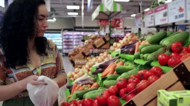 Marketteki genç kadın, olgun domatesleri raftan alır ve sepete koyar. Genç bir kadın süpermarketin bakkal bölümünden seçer..