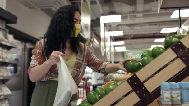 Aranyos nő választani friss zöldségek avokádó élelmiszerbolt. Fiatal nő választ a élelmiszer osztály egy szupermarket zöldség friss avokádó egy polcról, és teszi őket a kosárba. — Stock videók