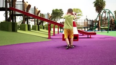 Mutlu çocuk salıncakları parkta sallanıyor, küçük çocuk, güneşli bir günde salıncakta sallanıyor, neşeli bir çocuk salıncağın hızını artırıyor, çocuk şehir parkında oynarken gülüyor ve gülümsüyor..