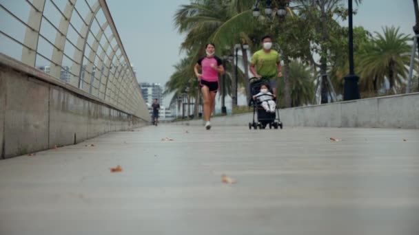 Sport familie koppel loopt samen in het park, jonge vader loopt met een baby liggend in een kinderwagen. Jongeren rennen samen op outdoor fitness training. Saigon, Vietnam, 6 april 2022 — Stockvideo