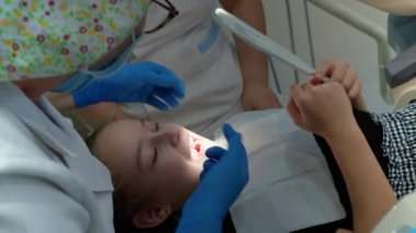 Kadın dişçi, klinikteki küçük bir kızın bebek dişlerini muayene ediyor. Kadın profesyonel dişçi iş başında. Diş muayenesi konsepti. Çocuklarla çalışan dişçi. Sağlık ve Tıp Konsepti.