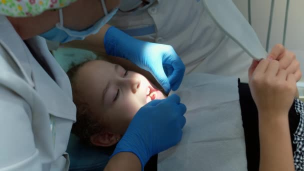 Dentysta przed usunięciem, wiatry nici dentystycznej na mleczny ząb małej dziewczynki kliniki.Kobieta profesjonalny dentysta w pracy.Dental checkup koncepcja. Dentysta pracuje z dziećmi. Koncepcja medycyny — Wideo stockowe