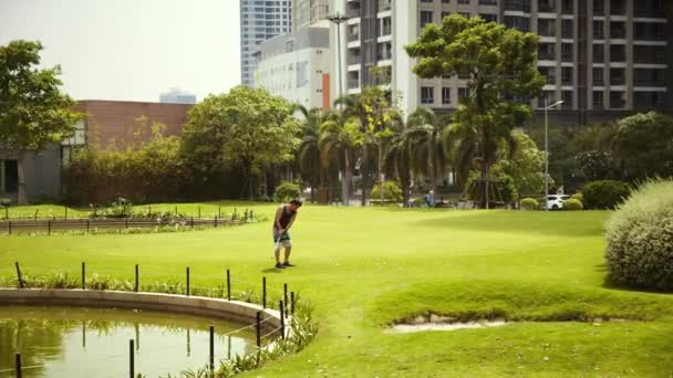 Uomo che gioca a golf sul campo da golf in città, oscillando e colpendo pallina da golf al rallentamento.Saigon River nel centro di Ho Chi Minh City, vicino al Vincom Central Park. Saigon, Vietnam, 6 aprile 2022 — Video Stock