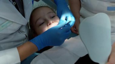 Kadın dişçi, klinikteki küçük bir kızın bebek dişlerini muayene ediyor. Kadın profesyonel dişçi iş başında. Diş muayenesi konsepti. Çocuklarla çalışan dişçi. Sağlık ve Tıp Konsepti.