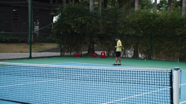 Asian mans dressed in tennis blue suits spending time on court,playing tennis on sunny day,holding a tennis racket,hitting a tennis ball in slow motion.Asia, Saigon,Vietnam, April 6, 2022 — Stock Video