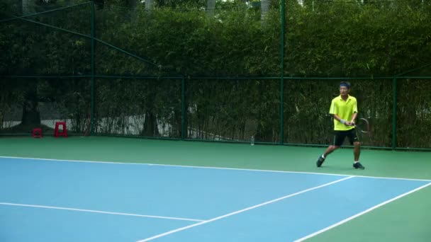 Azjaci ubrani w granatowe stroje tenisowe spędzają czas na korcie, grając w tenisa w słoneczny dzień, trzymając rakietę tenisową, uderzając piłkę tenisową w zwolnionym tempie. — Wideo stockowe