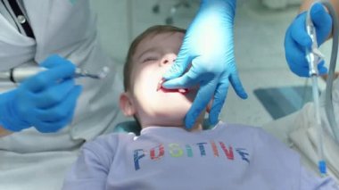 Kadın dişçi, klinikteki küçük bir çocuğun bebek dişlerini muayene ediyor. Kadın profesyonel dişçi iş başında. Diş muayenesi konsepti. Çocuklarla çalışan dişçi. Sağlık ve Tıp Konsepti.