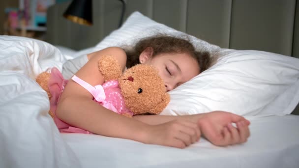 Zes jaar oud meisje slaapt lief in zijn wieg en lacht in zijn slaap. Close-up gezicht van een slapende baby op zijn zij. Tracking schoot slapende baby om middernacht. Slapen baby in bed. — Stockvideo