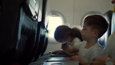 Uçakta uçarken uçak penceresinde oturan ve kağıt uçakla oynayan çocuklar. Childs 'ın eli uçak penceresinin arka planında küçük kağıt uçakla.