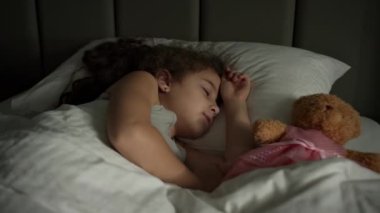 Küçük kız bebek onun beşiğinde tatlı tatlı uyuyor ve uykusunda gülümsüyor. Yan yatmış uyuyan bir bebeğin yakın plan yüzü. İzleme, gece yarısı uyuyan bebeği vurdu. Yatakta uyuyan bebek.