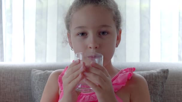 유리를 마시는 귀여운 소녀 신선 한 투명 한 물을 집에서 마실 수있다. 천천히 움직이는 작은 소녀는 물을 마신다. 어린이 음주 컵 건강 한 신체 관리를 클로즈업. 건강 한 생활 방식의 자녀들 — 비디오