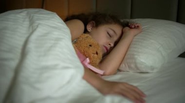 Altı yaşında bir kız çocuğu onun beşiğinde tatlı tatlı uyuyor ve uykusunda gülümsüyor. Yan yatmış uyuyan bir bebeğin yakın plan yüzü. İzleme, gece yarısı uyuyan bebeği vurdu. Yatakta uyuyan bebek.