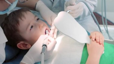 Kadın dişçi klinikteki küçük bir çocuğun bebek dişlerini muayene ediyor. Kadın profesyonel dişçi iş başında. Diş muayenesi kavramı.