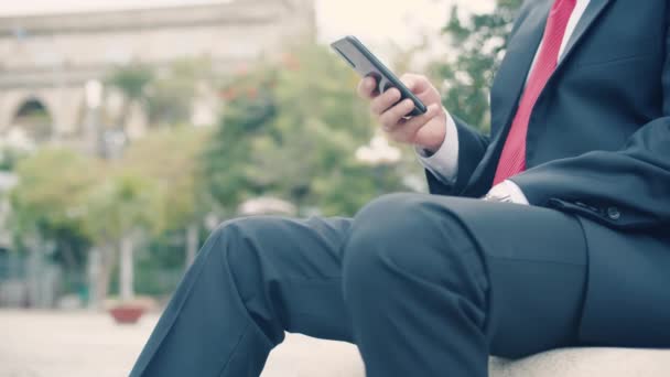 Großaufnahme Porträt Ernsthafter bärtiger Mann im teuren Anzug tippt etwas auf sein Handy, während er draußen auf einer Parkbank sitzt — Stockvideo
