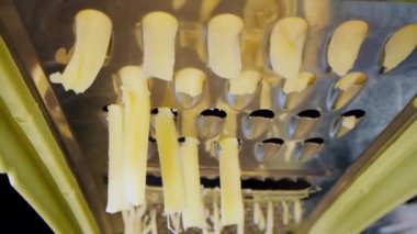 Izgara peyniri kapat, makro atış. Metal rendenin içindeki çerçeveyi çek. Ağır çekimde rendelenmiş peynir. Kadın, siyah arka planda izole edilmiş metal rendeyle peynir öğütüyor.