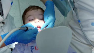 Kadın dişçi, klinikteki küçük bir çocuğun bebek dişlerini muayene ediyor. Kadın profesyonel dişçi iş başında. Diş muayenesi konsepti. Çocuklarla çalışan dişçi. Sağlık ve Tıp Konsepti.