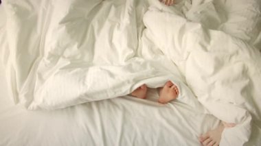 Çift yatakta ütü yapıyor. Sadece çerçevedeki bacaklar. Seninki battaniyenin altından uyanıyor. Baba, anne ve çocuğun bacakları öne çıkıyor. Evlilik, aile, aşk, çocuk konsepti. Sabah üçte yatakta.