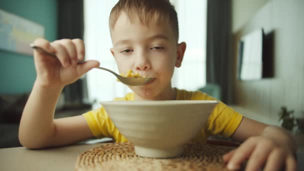 Retrato niño hambriento lindo niño se sienta en la mesa, come hojuelas de maíz con leche con apetito de placer, disfruta del desayuno. — Vídeos de Stock